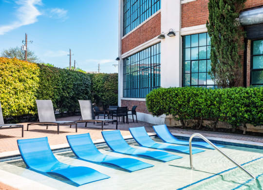 a pool with blue chaise lounge chairs in front of a brick building