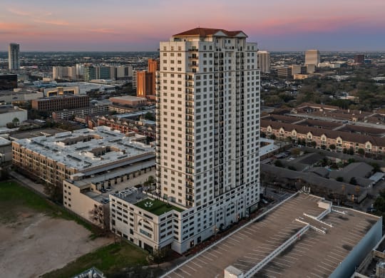 an aerial view of a tall building with a red roof and a parking lot in front of at Dominion Post Oak in Houston, TX