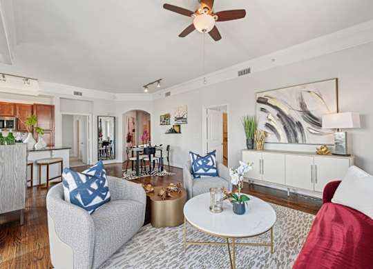Model living room with a grey couch, a red couch, a white coffee table, and a ceiling fan at Dominion Post Oak apartments in Houston, TX