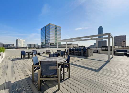 Wooden deck with chairs and a table with a metal frame on the rooftop patio at Dominion Post Oak apartments in Houston, TX