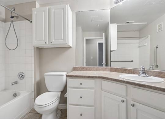 Edinburgh bathroom with a toilet, counter, sink, and mirror at Encore at Buckingham Apartments in Richardson, TX