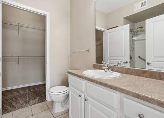 Edinburgh bathroom with a toilet, sink, and mirror at Encore at Buckingham Apartments in Richardson, TX