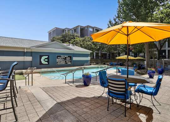A pool area with chairs and a yellow umbrella at Encore at Buckingham Apartments in Richardson, TX