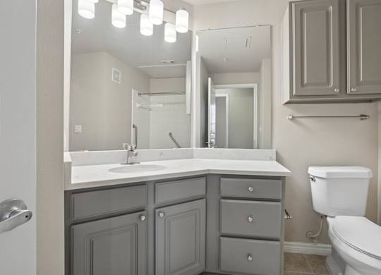 Kenzington bathroom with a white toilet and a sink with a mirror above it at Encore at Buckingham Apartments in Richardson, TX