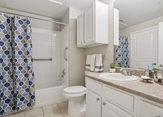 Windsor bathroom with a white toilet and a shower curtain and a sink at Encore at Buckingham Apartments in Richardson, TX