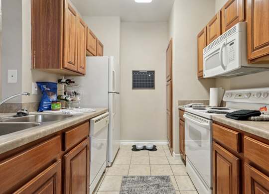 Windsor kitchen with wooden cabinets and white appliances at Encore at Buckingham Apartments in Richardson, TX
