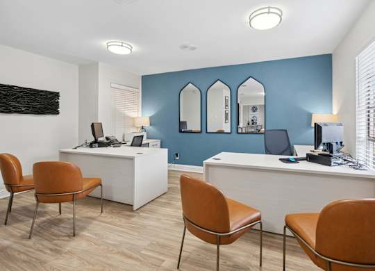 A room with a white desk and orange chairs.