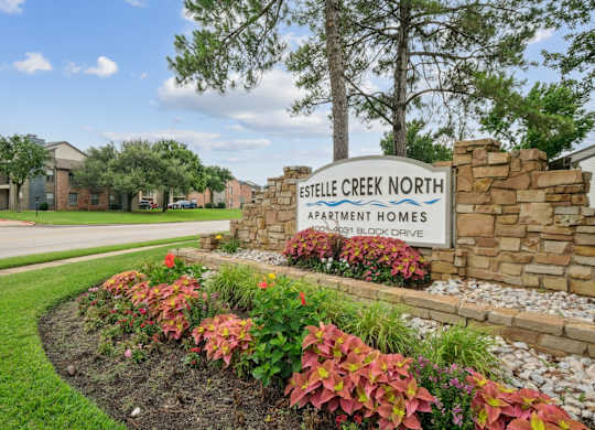 A sign for Estelle Creek North Apartment Homes sits in front of a flower bed.