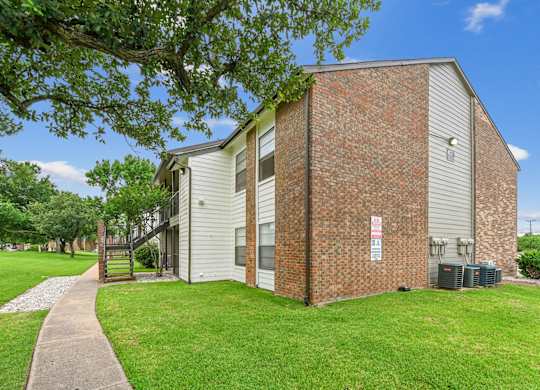 An apartment building with white wood and brick siding is surrounded by a lush grassy area at Estelle Creek North Apartments in Irving, TX