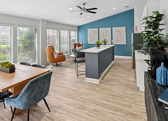 A modern clubhouse with comfortable seating, a ceiling fan, kitchen, and wood floors at Estelle Creek North Apartments in Irving, TX