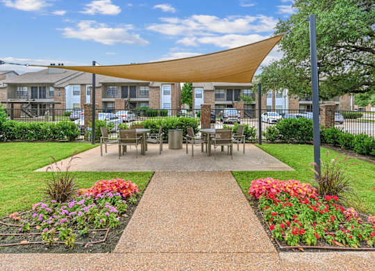 A sunny day at a park with a bench and a table under a shade structure.
