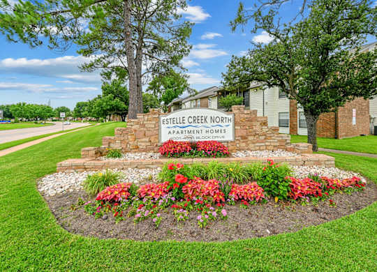 A sign for Estelle Creek North Apartment Homes is surrounded by flowers and greenery.