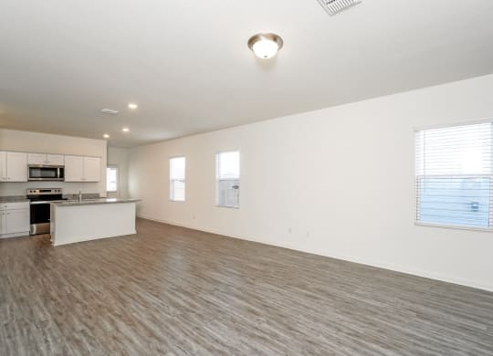 an empty living room with a kitchen in the background