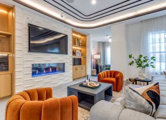 Clubhouse with a fireplace, television, and orange and gray seating at Era Apartments in Denton, TX
