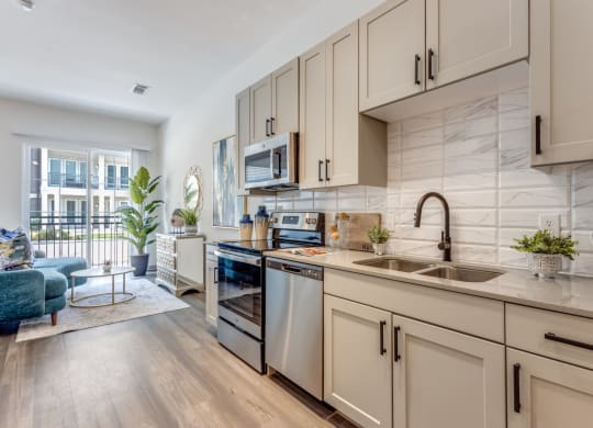 Model Studio kitchen with white cabinets and a sink and stainless steel appliances at Era Apartments in Denton, TX