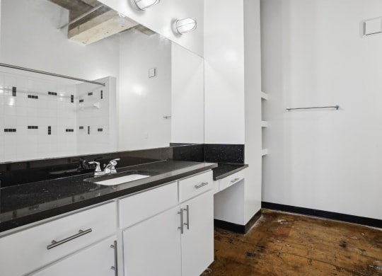 Farm and Ranch spacious bathroom with soaking shower tub, modern black countertop vanity, and built-in shelving | Deep Ellum Lofts in Dallas, TX