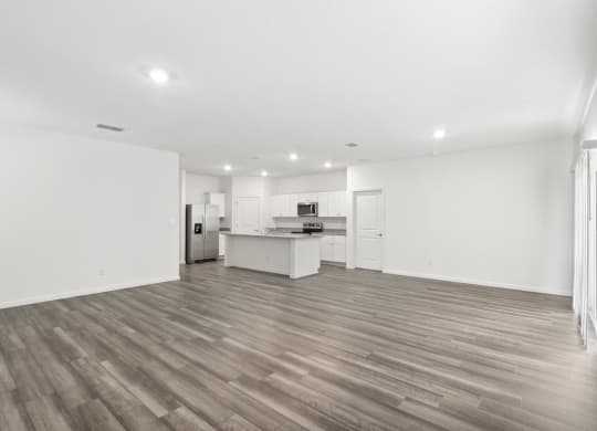 an empty living room with a kitchen in the background