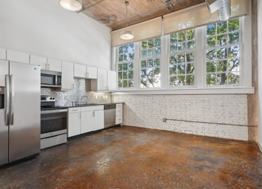 Futura Lofts kitchen with white cabinets and stainless steel appliances and large windows | Deep Ellum Lofts in Dallas, TX