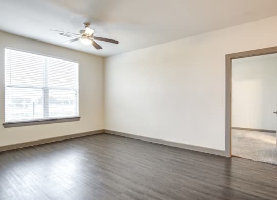 an empty living room with a window and a ceiling fan
