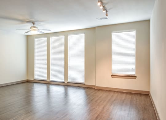 an empty living room with windows and wood floors and a ceiling fan