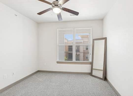 A bedroom with a ceiling fan, mirror, and a window with blinds at GreenVue Apartments in Richardson, TX