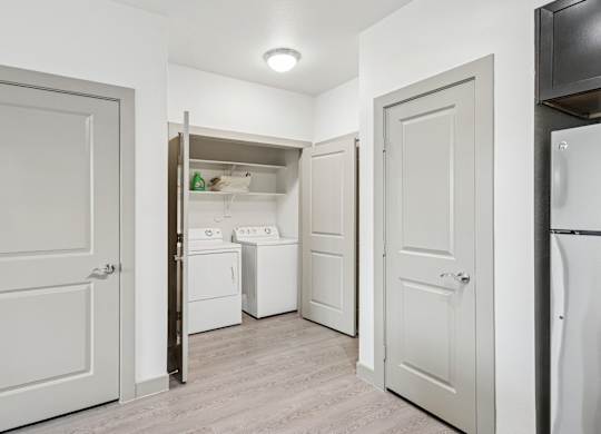 A dedicated laundry space with a full size washer and dryers and shelves at GreenVue Apartments in Richardson, TX
