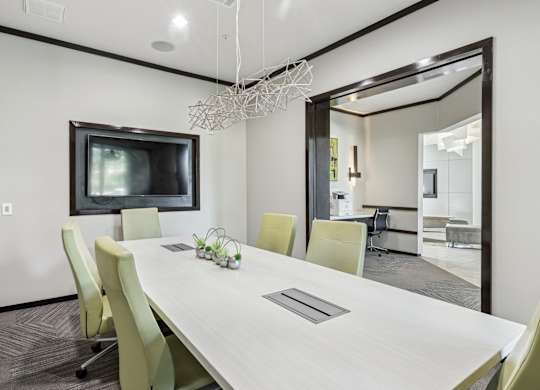 A modern conference room with a long table, chairs, and a television at GreenVue Apartments in Richardson, TX
