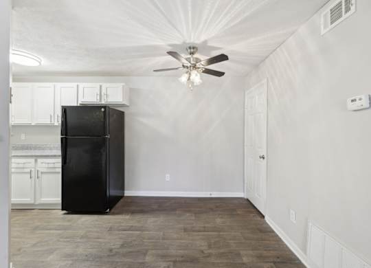 A black fridge in the kitchen leading to a dining area with a ceiling fan at Gwinnett Square Apartments in Duluth, GA