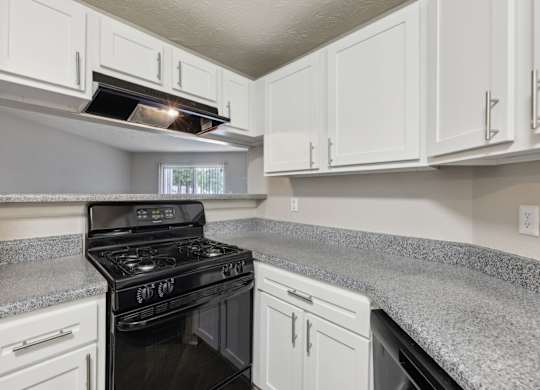 A black stove top oven in a kitchen with white cabinets at Gwinnett Square Apartments in Duluth, GA