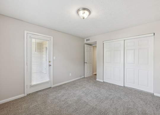 A bedroom with a carpeted floor, closet, and glass door leading to a balcony at Gwinnett Square Apartments in Duluth, GA
