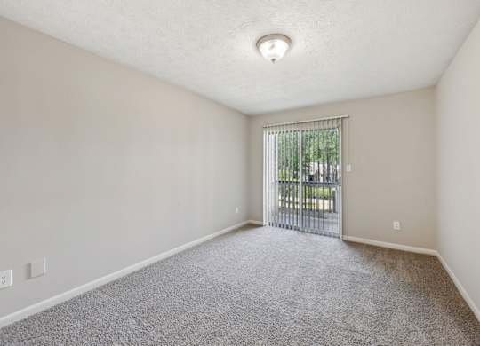 A room with a carpeted floor and a sliding glass door leading to a balcony at Gwinnett Square Apartments in Duluth, GA