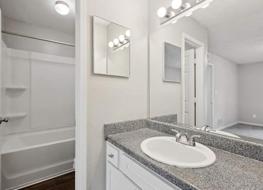 A bathroom with a sink, mirror, and a bathtub at Gwinnett Square Apartments in Duluth, GA