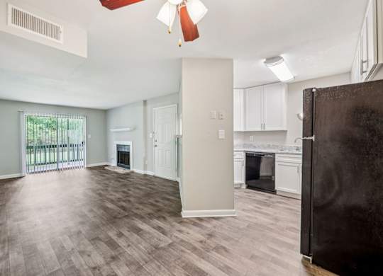 A kitchen and living area with a refrigerator, oven, and cabinets, fireplace, and glass doors leading to a balcony at Gwinnett Square Apartments in Duluth, GA