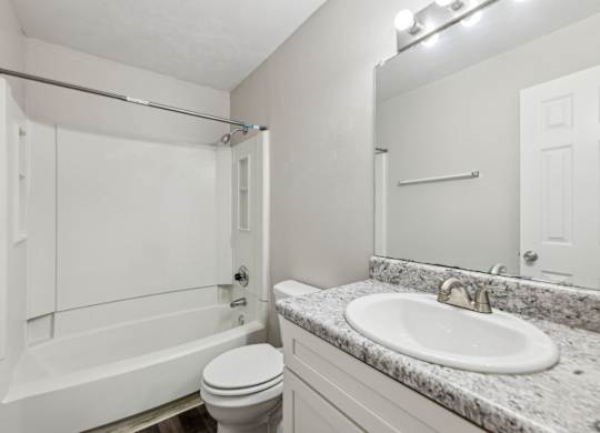 A white bathroom with a toilet, sink, mirror, and bathtub at Gwinnett Square Apartments in Duluth, GA