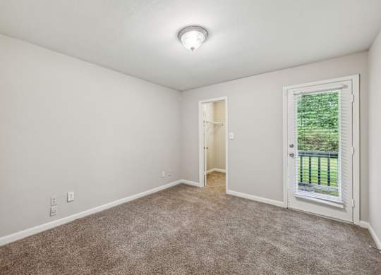 A bedroom with a carpeted floor and a door leading to a balcony at Gwinnett Square Apartments in Duluth, GA