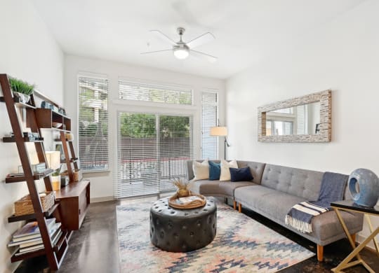 Model living room with a gray couch and a large doorway to patio at Harlow River Oaks in Houston, TX