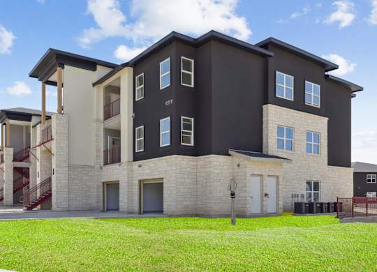 A modern apartment building with black and beige siding and a lush, grassy area in front at Hillside on Parmer Apartments in Austin, TX