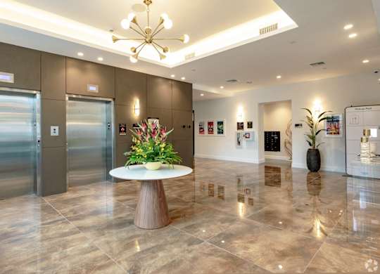 Lobby area with white table with a flower arrangement and elevators at Hollywood Heights on the Boulevard Luxury Apartments in Hollywood, FL