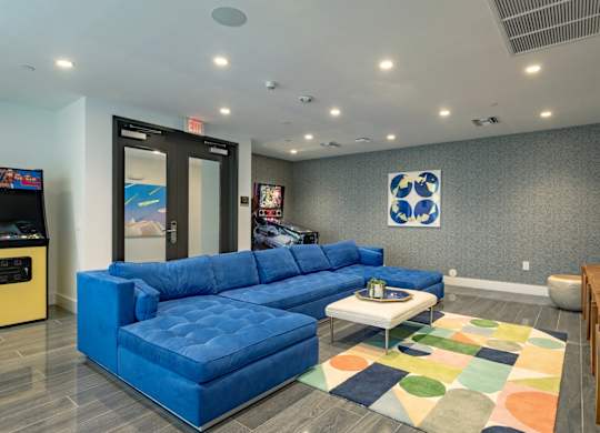 Our lounge and gaming zone with a blue sofa and arcade games at Hollywood Heights on the Boulevard Luxury Apartments in Hollywood, FL