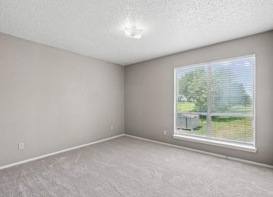 A bedroom with a window and a view of a green grass and trees outside at Heritage Square Apartments in Waco, TX