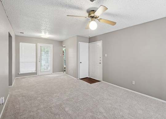 A living room with a ceiling fan and carpeted floor at Heritage Square Apartments in Waco, TX