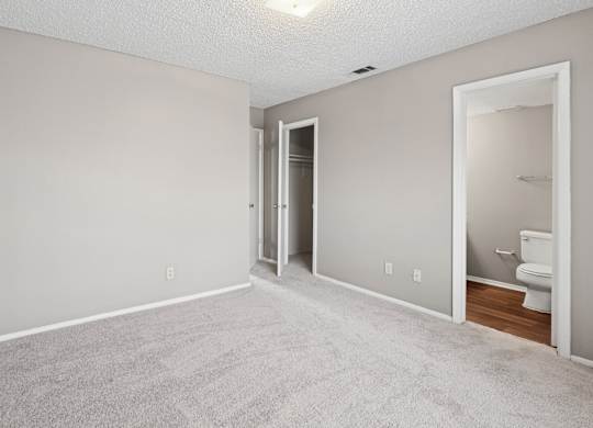A bedroom with a carpeted floor and a door to the bathroom at Heritage Square Apartments in Waco, TX