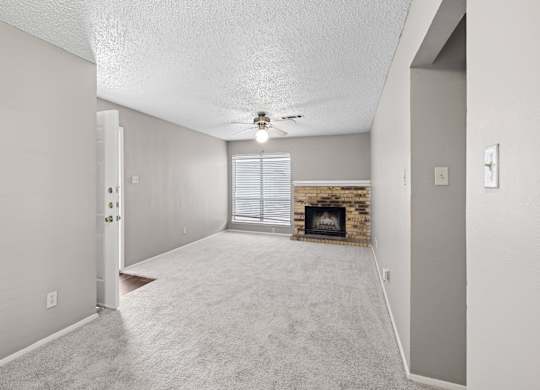 A spacious living room with a brick fireplace and a ceiling fan at Heritage Square Apartments in Waco, TX