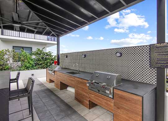 Outdoor grilling station with two BBQ grills, a sink, and ample seating under a pergola  Balcony view of Hollywood Boulevard at Hollywood Heights on the Boulevard Luxury Apartments in Hollywood, FL