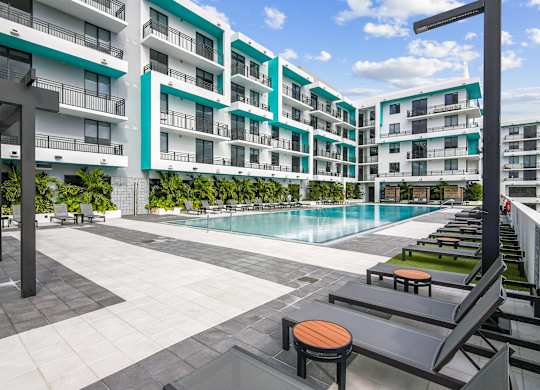 Patio lounge chairs surrounding our beautiful pool with lush greenery  at Hollywood Heights on the Boulevard Luxury Apartments in Hollywood, FL