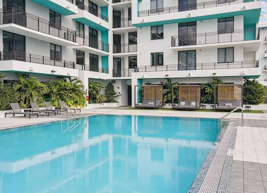 Cushioned lounge chairs and patio lounge chairs by our beautiful pool at Hollywood Heights on the Boulevard Luxury Apartments in Hollywood, FL