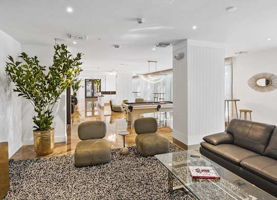 lounge area with brown chairs, a grey couch, and a green plant with our social club with a pool table in the background at Hollywood Heights on the Boulevard Luxury Apartments in Hollywood FL