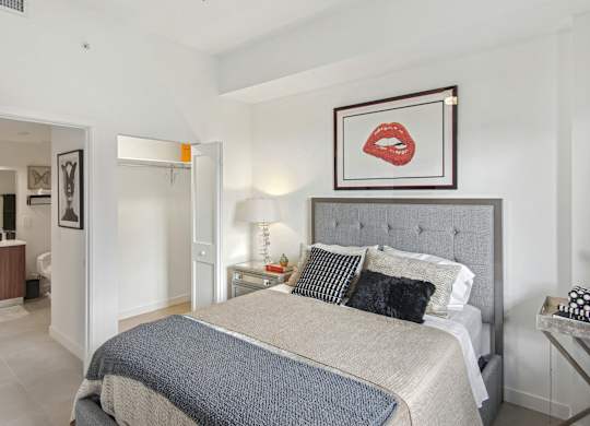 A bedroom with a bed, nightstand, and a picture of red lips above the bed at Hollywood Heights on the Boulevard Luxury Apartments in Hollywood, FL