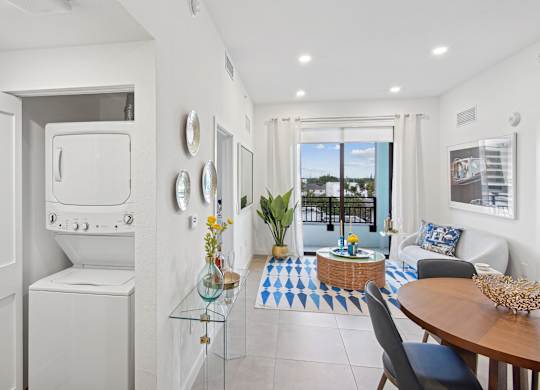 A modern living room with a dining table and chairs and a washer and dryer on the left at Hollywood Heights on the Boulevard Luxury Apartments in Hollywood, FL