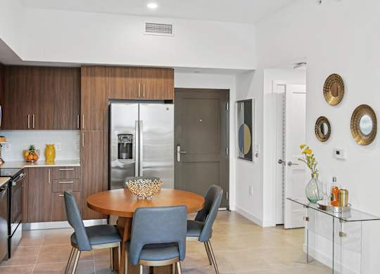 A modern kitchen with a dining table and chairs, fridge with a ice maker, stovetop, and microwave  Living room and modern kitchen in our 2-bedroom model with a dining table and chairs  Balcony view of Hollywood Boulevard at Hollywood Heights on the Boulevard Luxury Apartments in Hollywood, FL